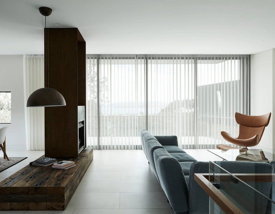 welcome westral About Us 1 Modern living room featuring Perth blinds, a blue sofa, a brown leather chair, a wooden bench, and a large window with a view.