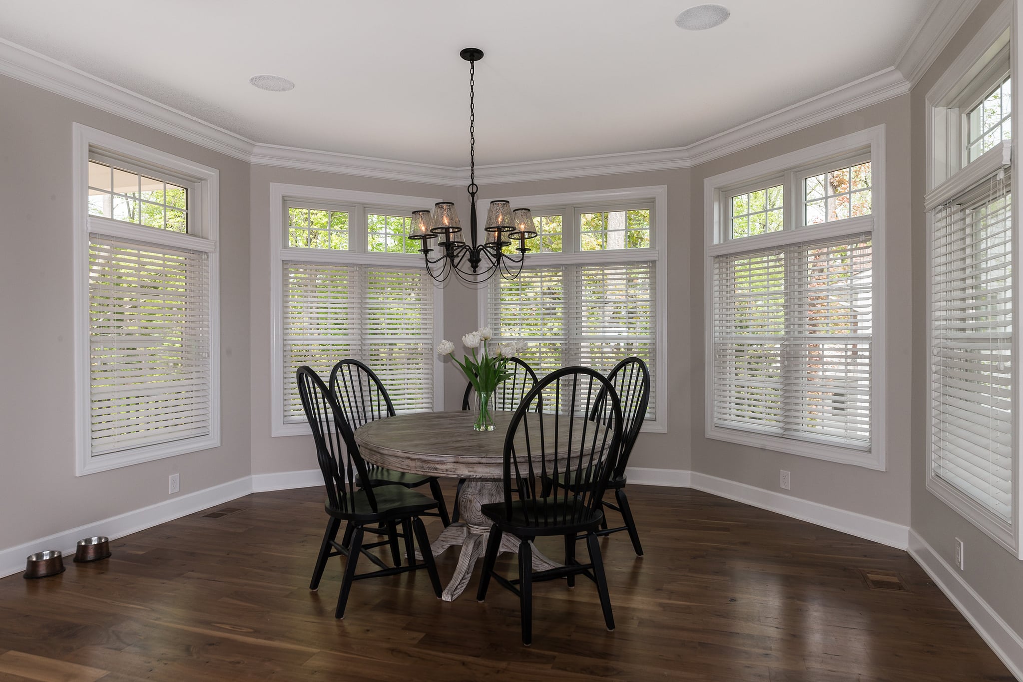 Dining room with energy saving windows, blinds, and shutters. Round table with chairs, chandelier, hardwood floor. Natural light.