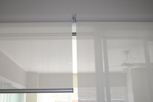 Close-up of white roller blinds partially unrolled, showcasing the material and mechanism. Benefits of roller blinds include light control.