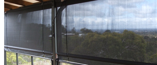 Verandah Awnings Verandah Awnings 1 Verandah awnings: Outdoor patio featuring dark grey mesh verandah awnings, providing shade and privacy while allowing a view of the landscape.