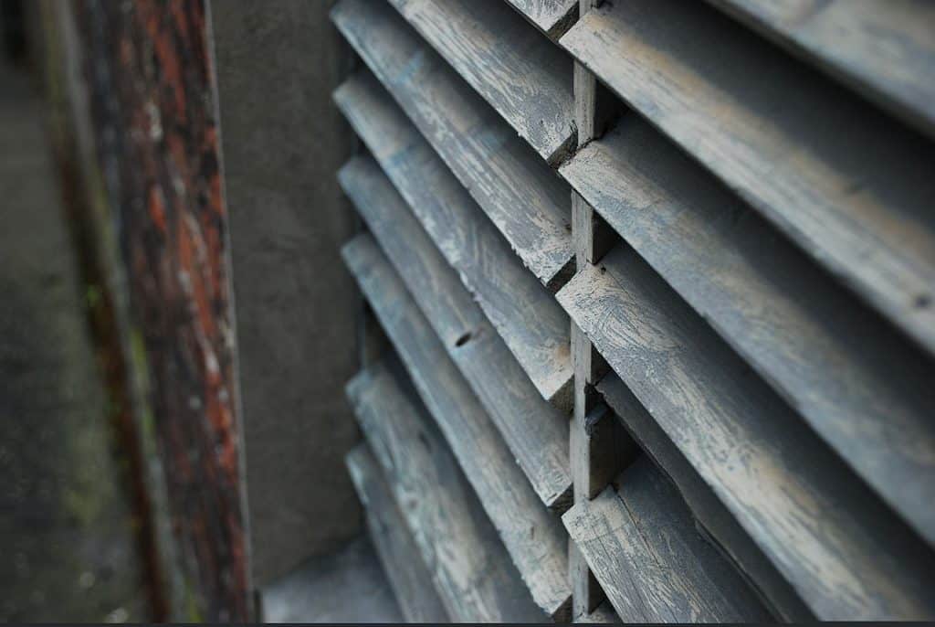 Close-up of wooden window shutters, an excellent investment for homes. Gray-washed louvers provide privacy and light control. #blinds #shutters