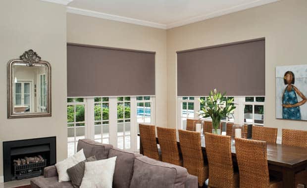 About Us: Stylish living room featuring brown roller blinds on windows, a dining table with wicker chairs, and a comfortable sofa.