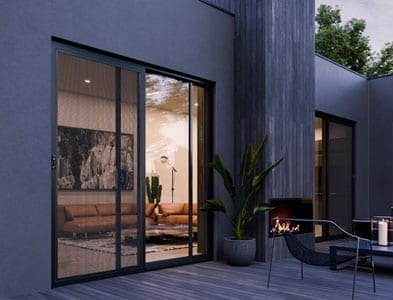 Modern home's outdoor community space with sliding glass doors, a fireplace, and stylish furniture. Interior living room visible through the glass.