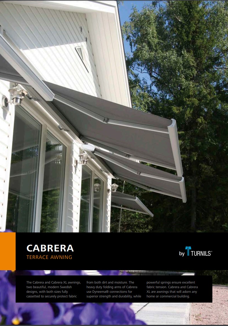Cabrera folding arm awning on a white house. The gray awning extends over windows, providing shade. Trees are visible in the background.